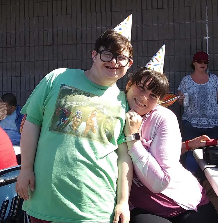 Two people in party hats lean on each other and smile